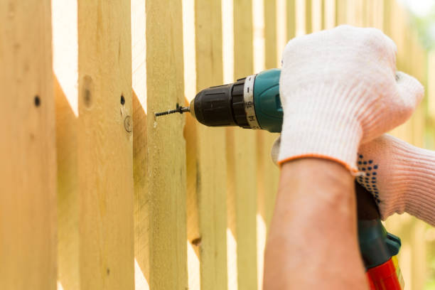 A person drilling a hole in a wood fence
